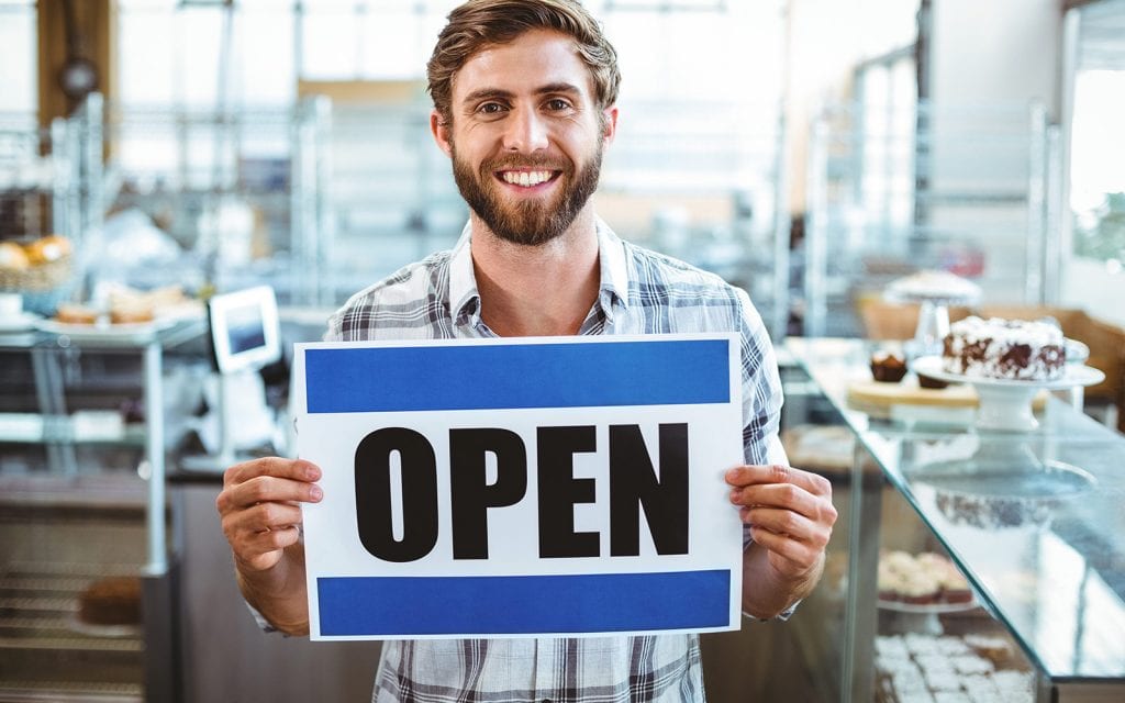 Smiling man holding open sign for his business