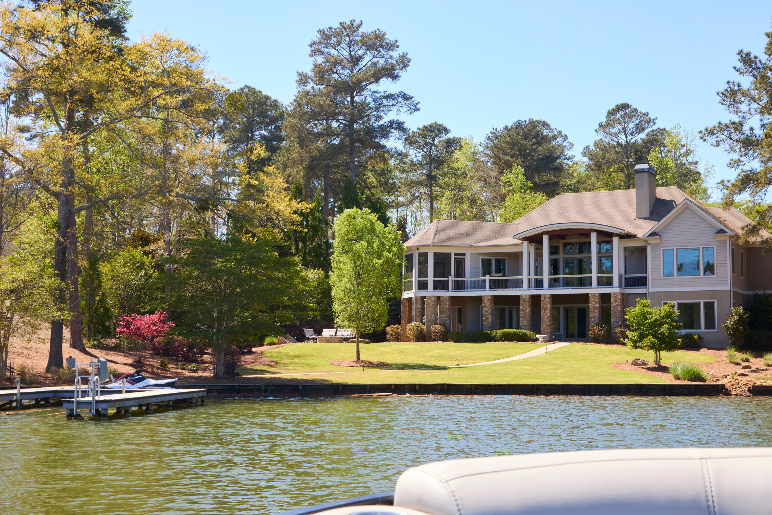 A beautiful two-story contemporary lake house with a dock and lush green lawn on a sunny day maryland waterfront property ownership